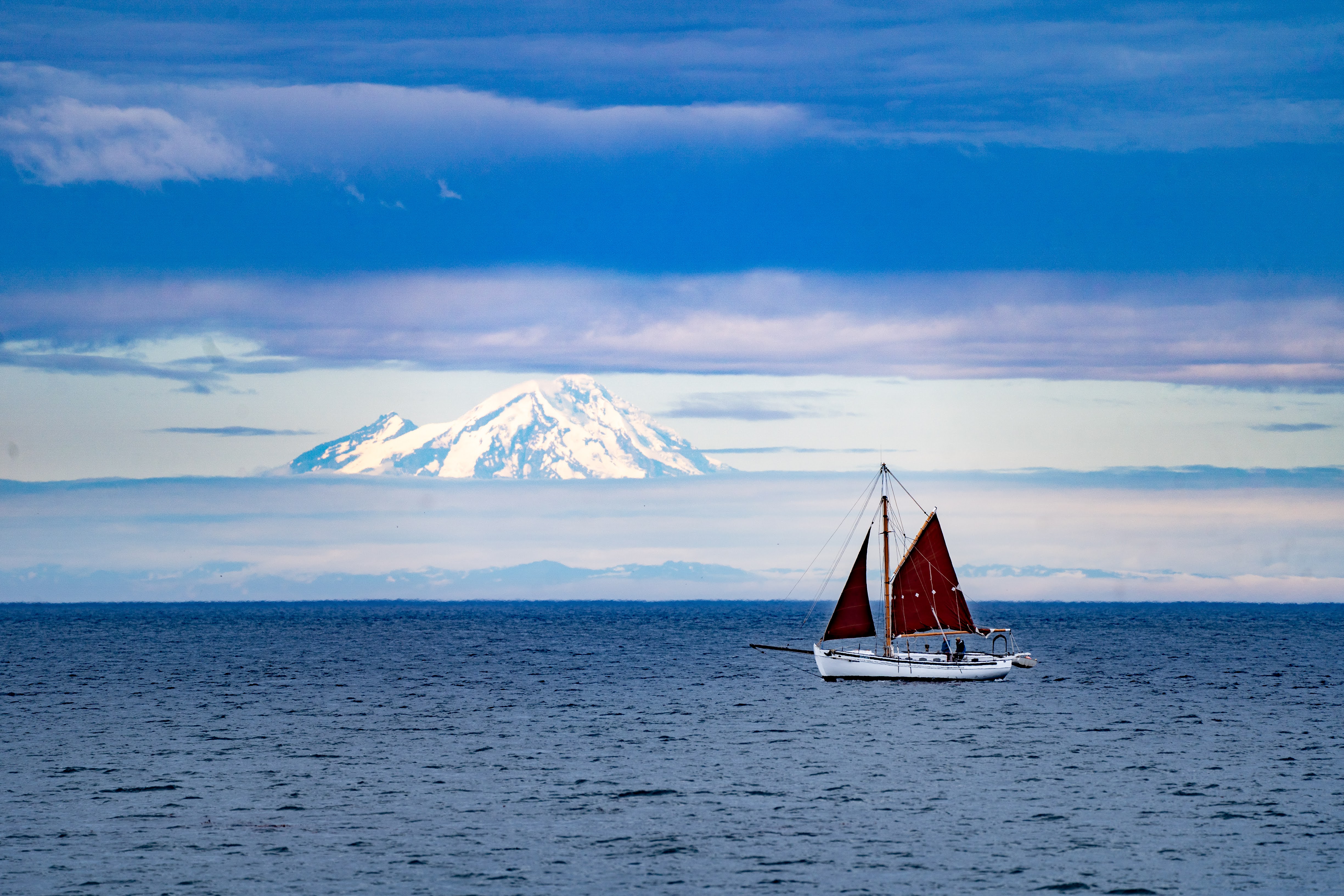 Red-sailed sailboat on Kachemak Bay with Mt. Redoubt volcano in the distance